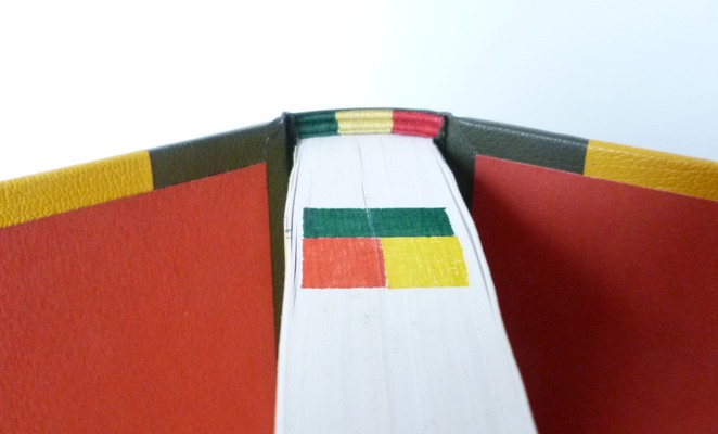 Demi-cuir vert, collé à celui-ci 2 rectangles superposés jaune et rouge, le tout représentant à droite ou à gauche le drapeau béninois. Tranchefile tricolore reprenant le drapeau béninois que l'on retrouve aussi sur la tranche de tête.