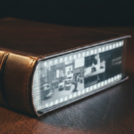 Une vue rapprochée d'une reliure posée sur une table en cuir dont la tranche se transforme progressivement en une pellicule de film 35mm transparente.